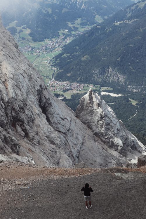Free A lone hiker stands on a cliff edge overlooking a scenic mountain valley. Stock Photo