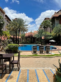 Beautiful resort pool surrounded by palm trees, tables, and chairs under a clear blue sky.