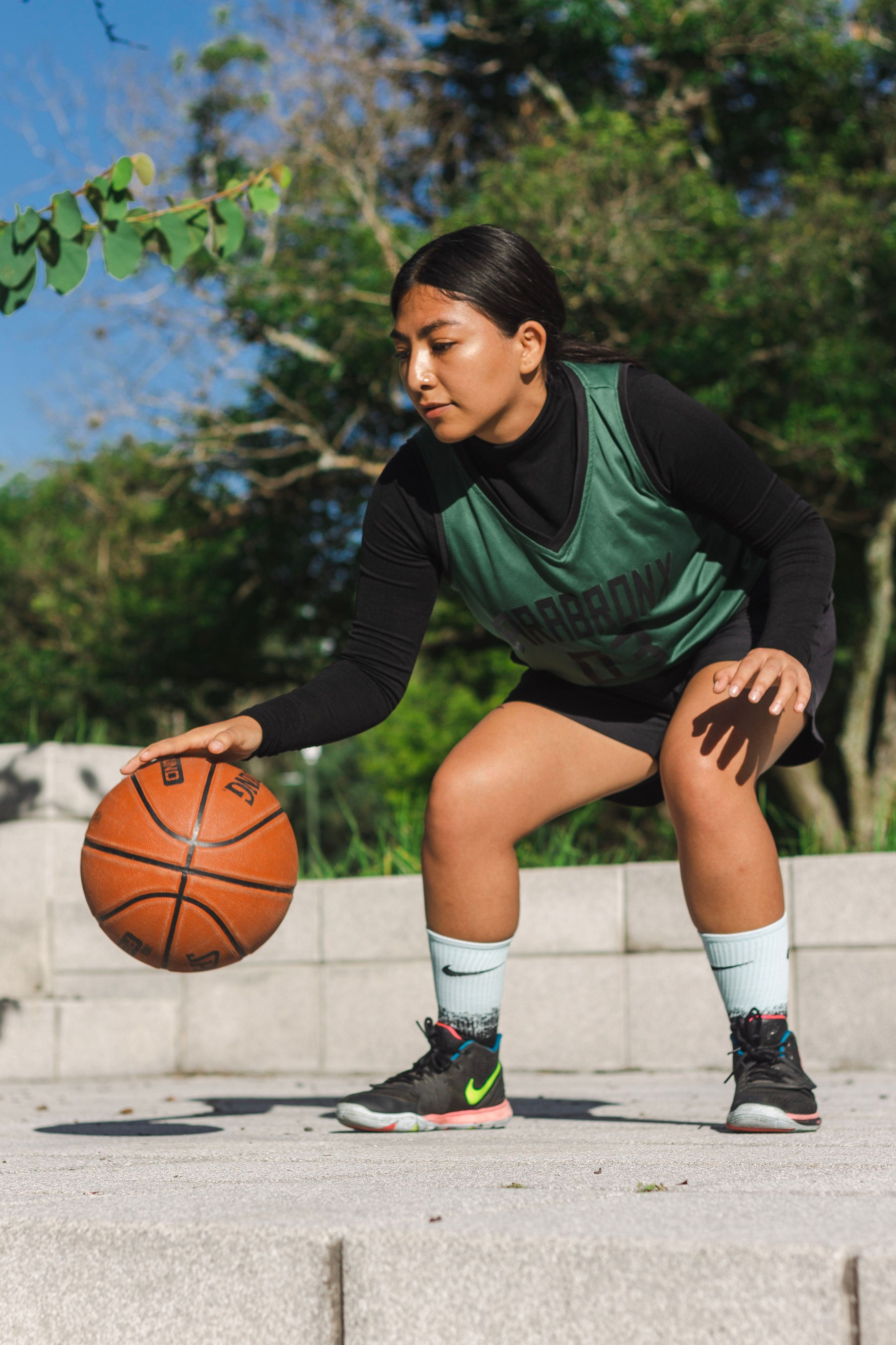 A woman dribbles a basketball outdoors on a sunny day, showcasing athletic skills.