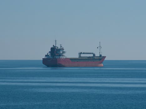A red cargo ship navigates across calm blue sea, showcasing maritime transport.