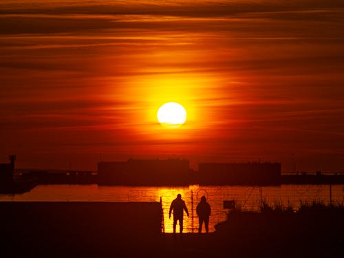 Silhouette of People standing at the Seashore during Sunset