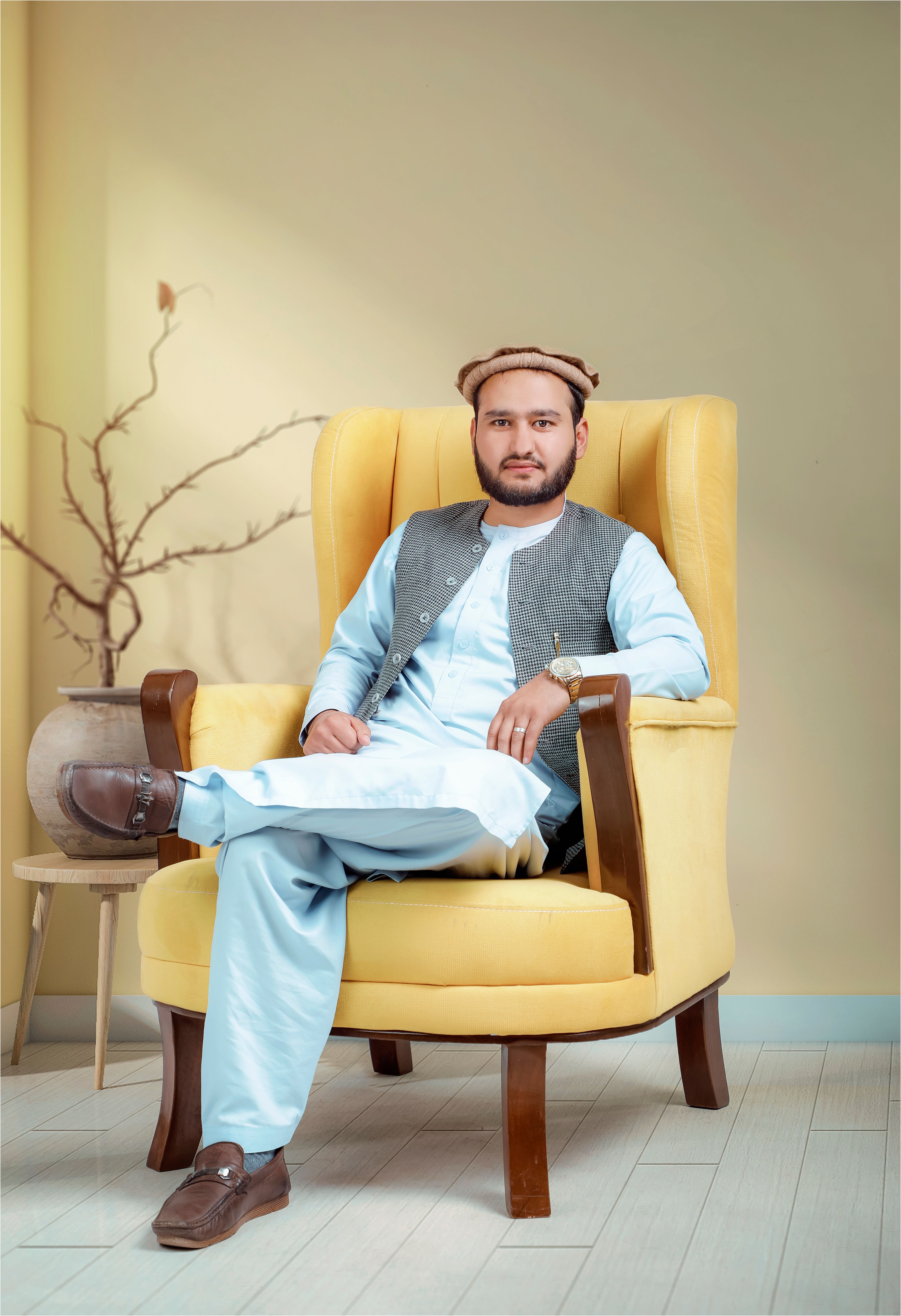 Man in traditional attire sitting in a yellow armchair indoors, exuding relaxation and confidence.