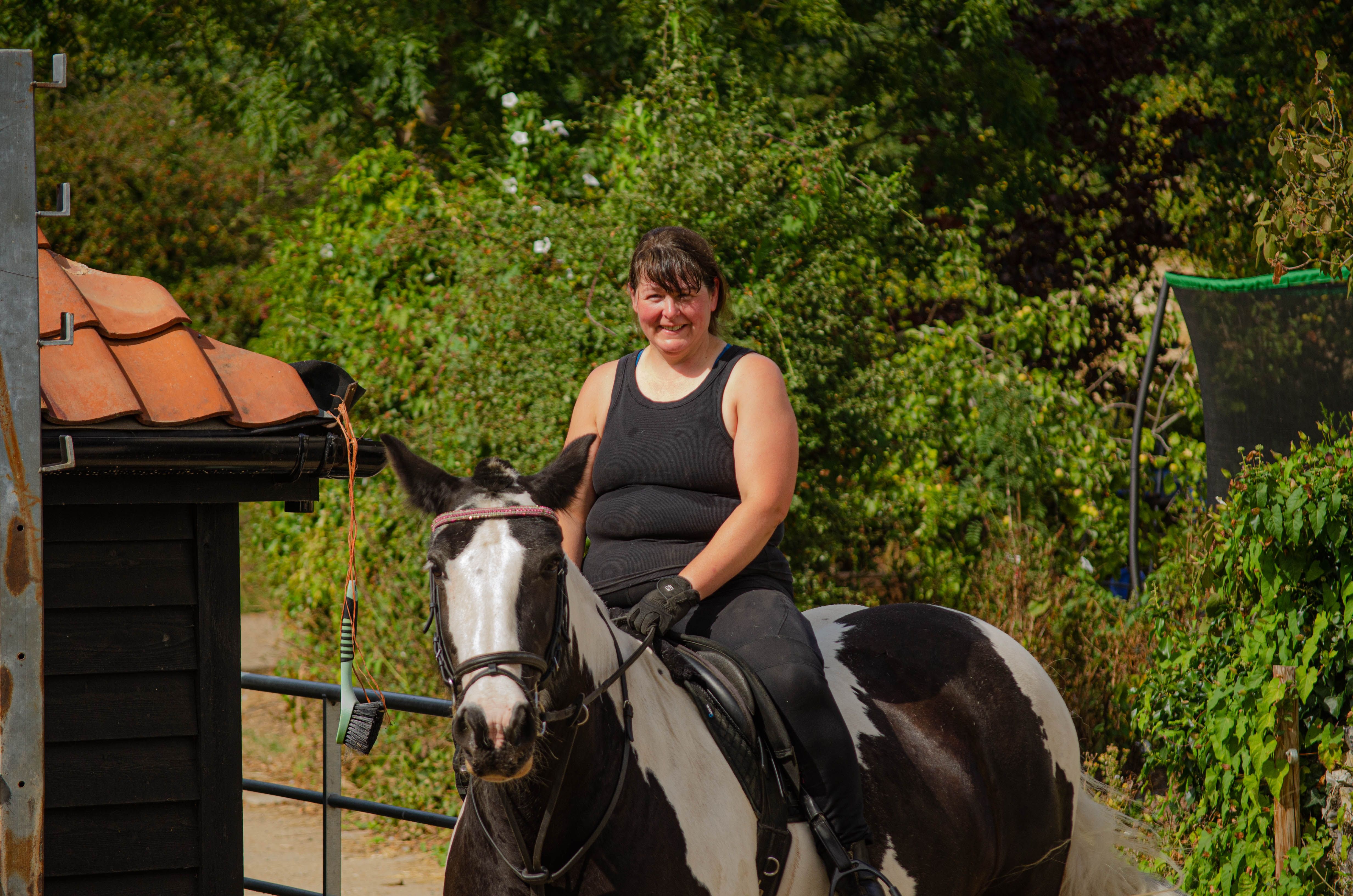Woman enjoying horseback riding outdoors, smiling amidst lush greenery.