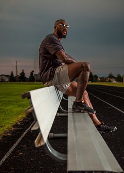 Man sitting on a bench near a running track at twilight, enjoying the calm.