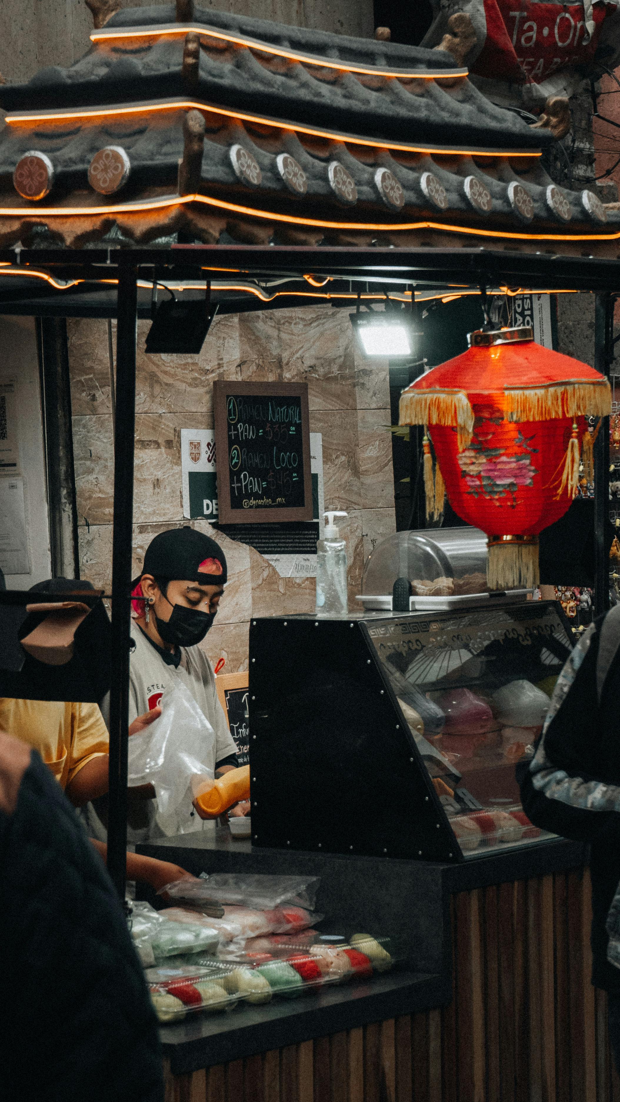Asian street vendor preparing food at an outdoor market with traditional decor and a vibrant atmosphere.