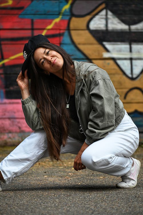 Woman Wearing a Gray Jacket and White Pants Crouching on the Ground