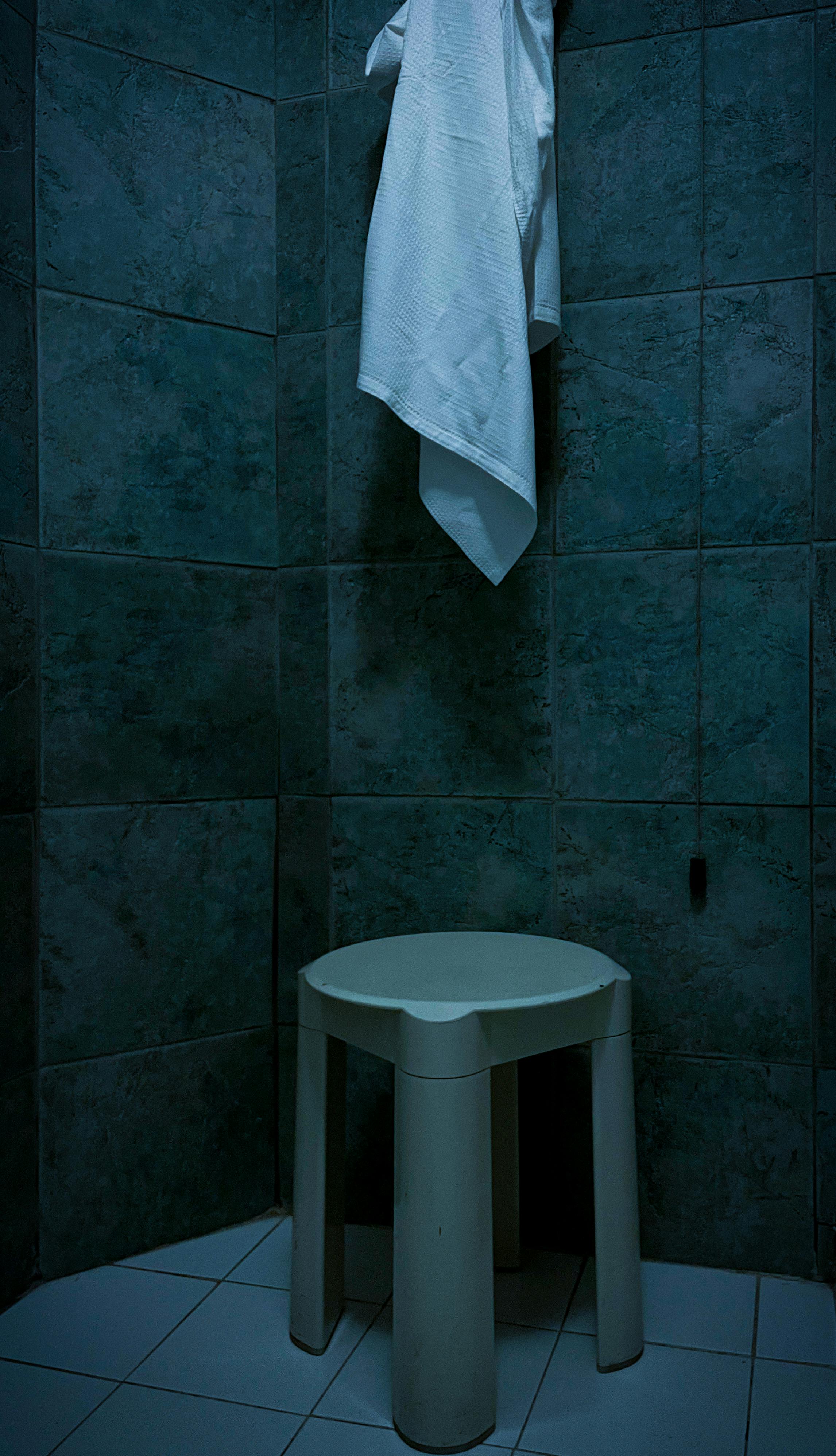 A simple bathroom setting in Italy featuring a towel and stool against a tiled wall.