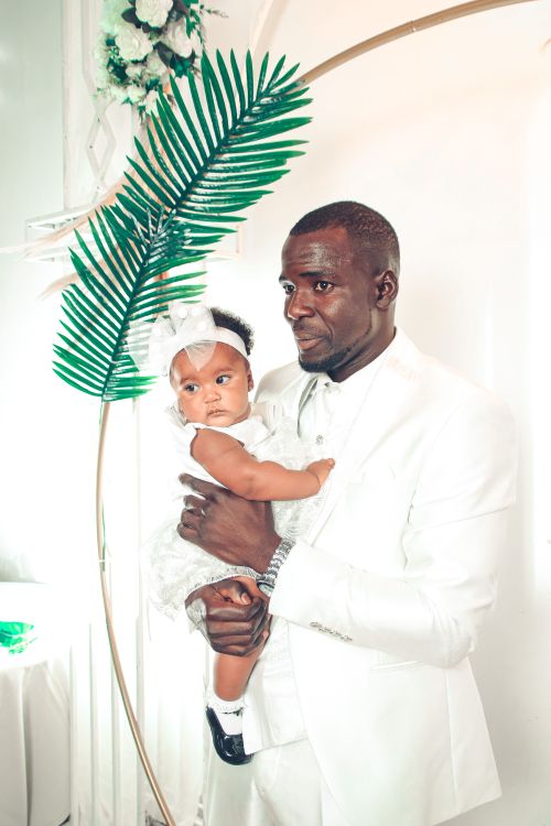Free Elegant father holding daughter in white at indoor ceremony with floral decor. Stock Photo