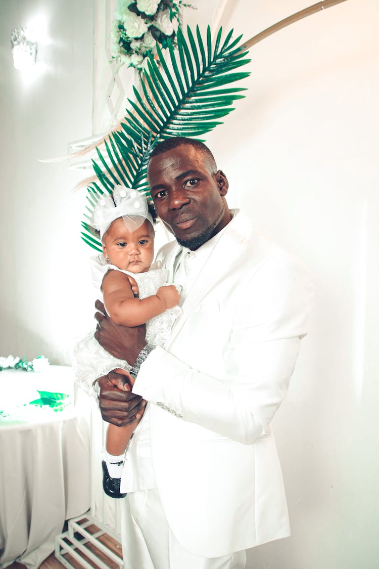 A Man In A White Suit Carrying A Baby