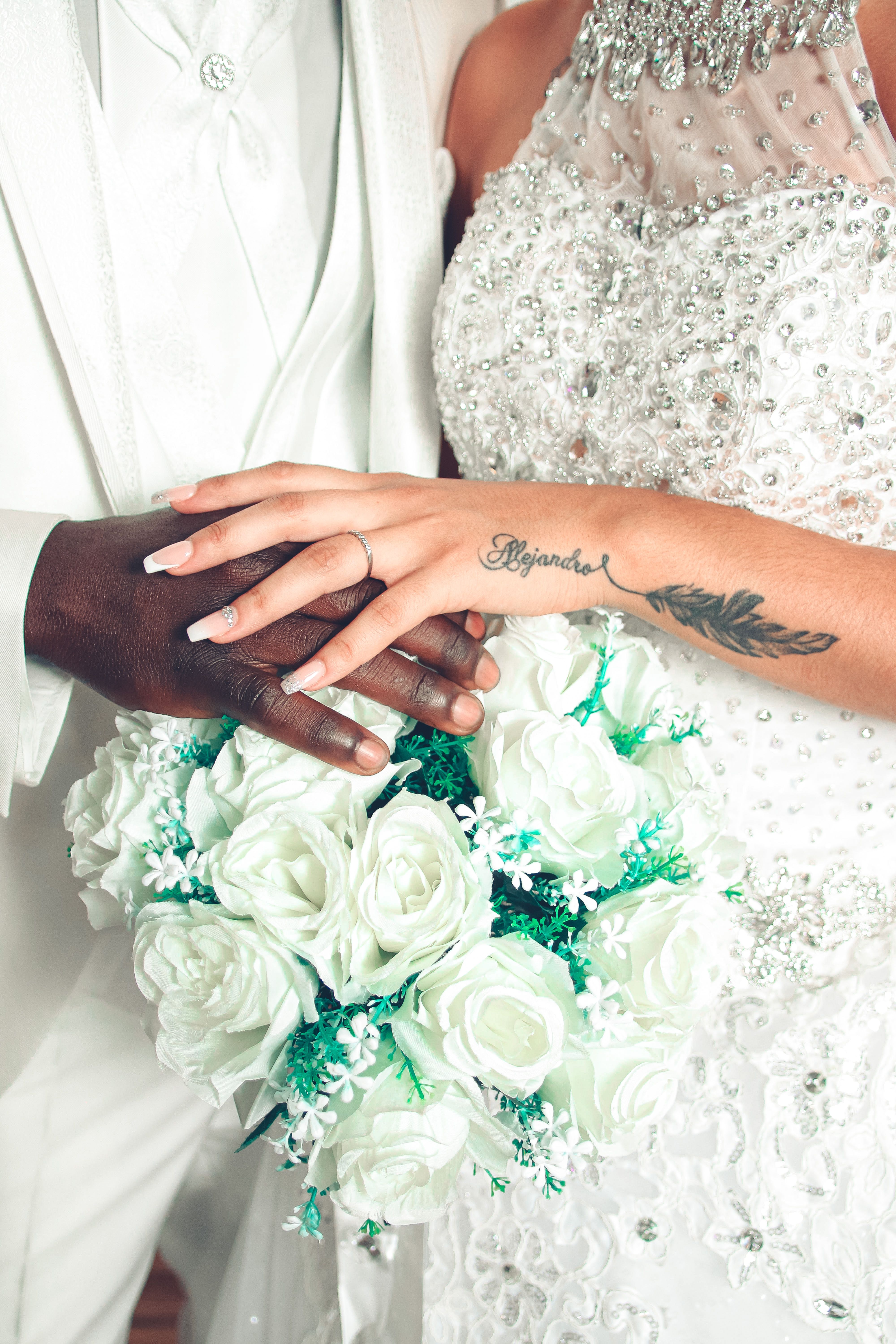Close-up of a bride and groom's hands with white rose bouquet highlighting love and unity.