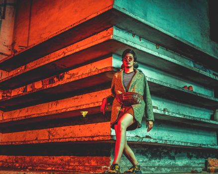 Fashionable woman in sunglasses leans against colorful urban wall, embodying style and attitude.