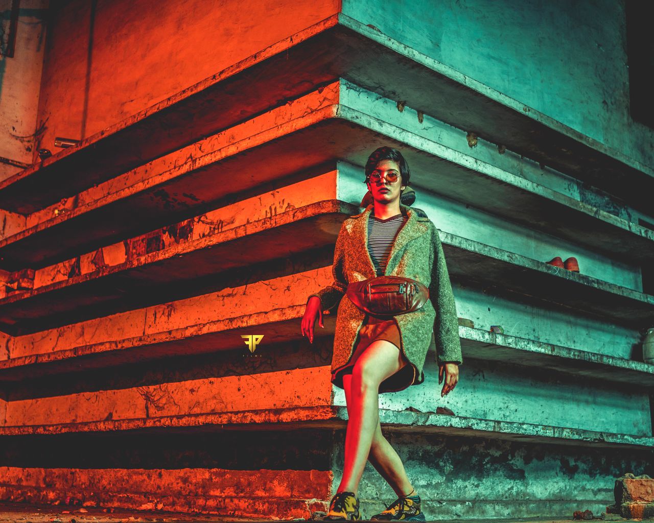 fashionable woman in sunglasses leans against colorful urban wall embo