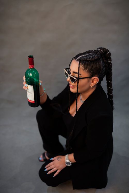 Free Stylish woman in black with braids holds red wine, showcasing modern fashion in Tehran studio. Stock Photo