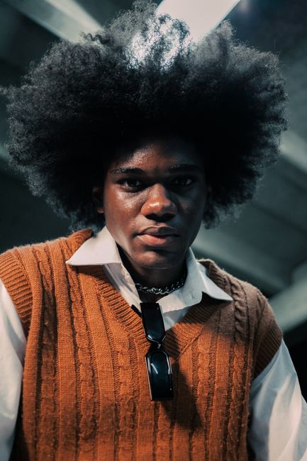 Portrait of a fashionable man with afro hair wearing a brown knitted vest indoors.