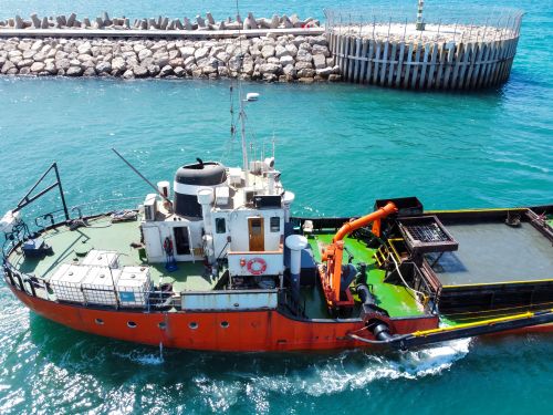 Free Drone shot of a vibrant fishing boat navigating a sunny coastal harbor. Stock Photo