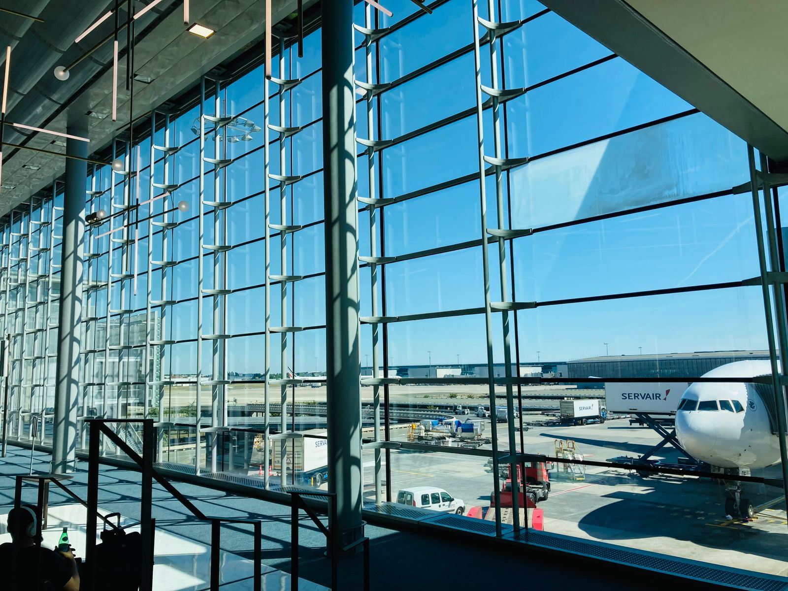 A spacious airport terminal with a glass facade overlooking an aircraft on the tarmac