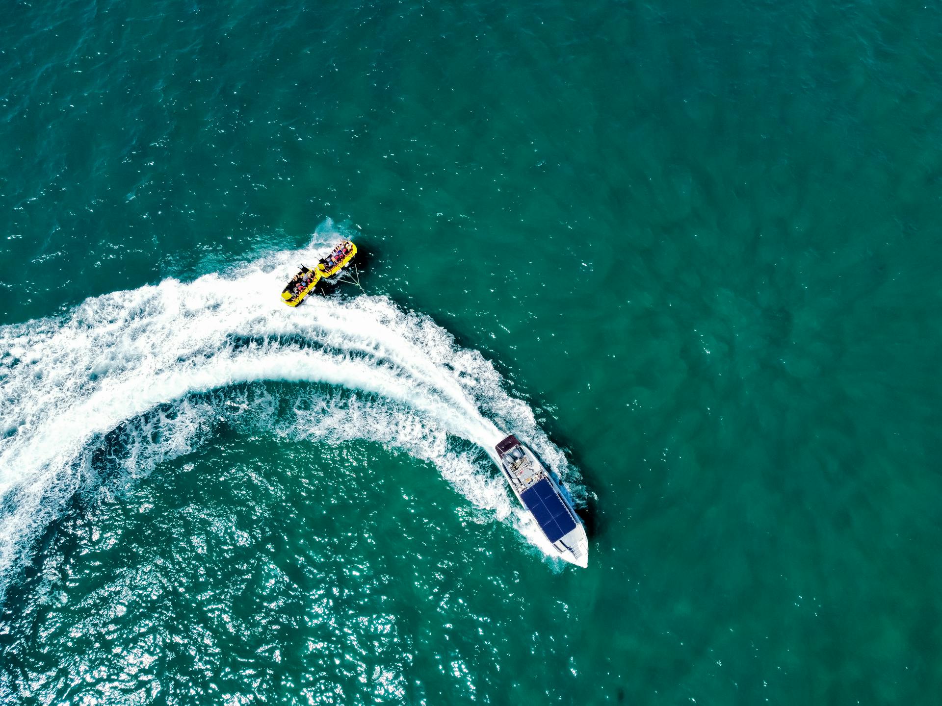 Dynamic aerial shot of a motorboat towing an inflatable raft over crystal clear blue waters.