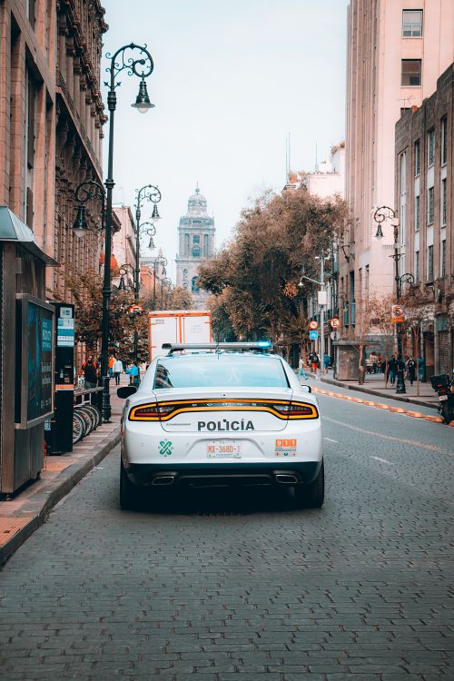 Free A police car is parked on a cobblestone street in a historic city with architecture and street lamps. Stock Photo