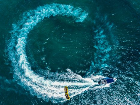 Aerial shot of a speedboat towing a tube, creating a circular wave pattern on the ocean's surface.