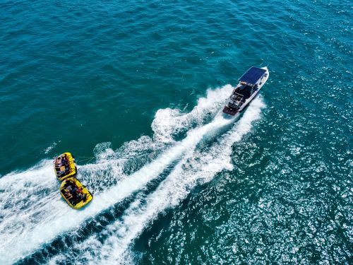 Free A thrilling aerial view of a motorboat towing inflatable rafts on the ocean, ideal for water adventure enthusiasts. Stock Photo