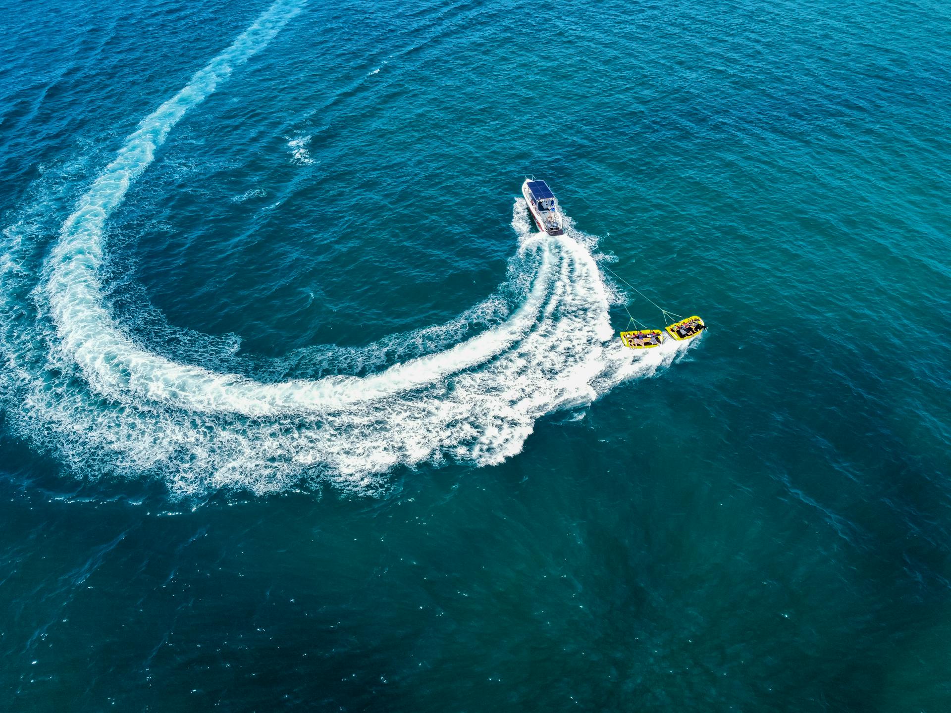 A drone captures a motorboat towing an inflatable raft on vast ocean waters.