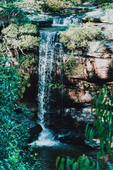 A serene waterfall flowing through rocks surrounded by vibrant green foliage in a tranquil forest setting.