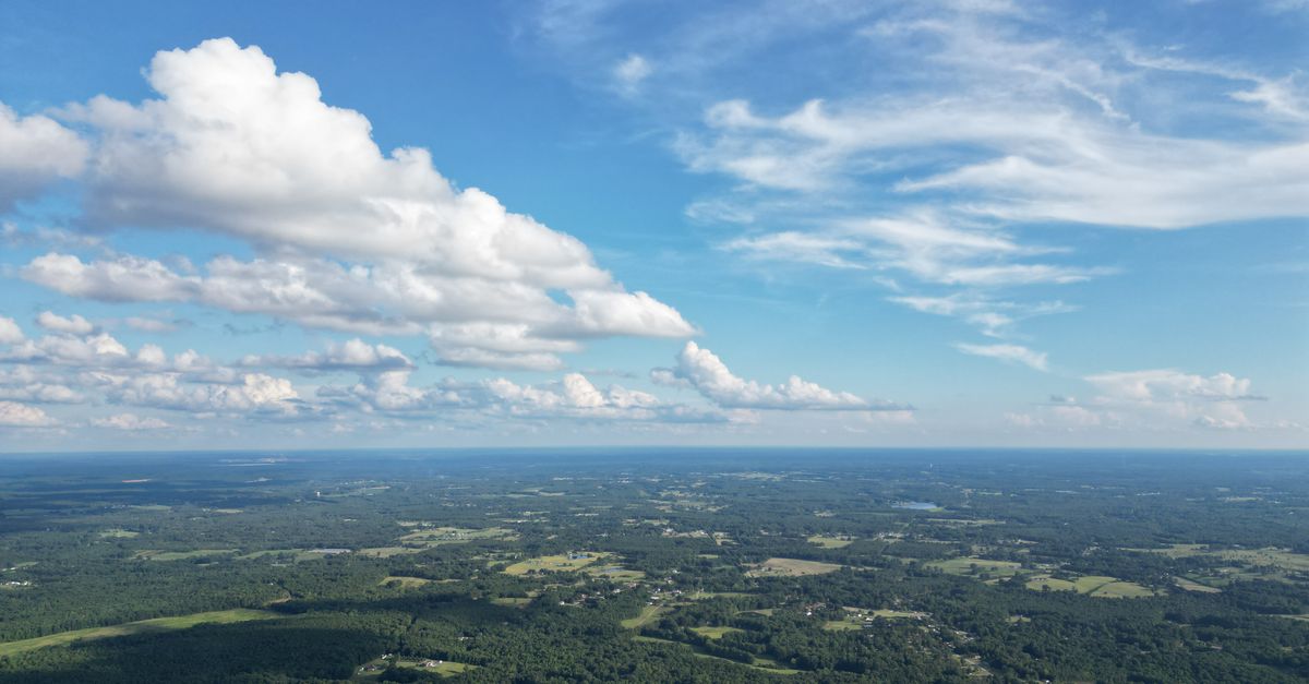 Drone-captured scenic aerial view of lush green landscapes and blue sky with white fluffy clouds in Lancaster, SC.