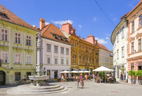 Free Vibrant square in Ljubljana featuring historic architecture, a fountain, and lively street cafes. Stock Photo