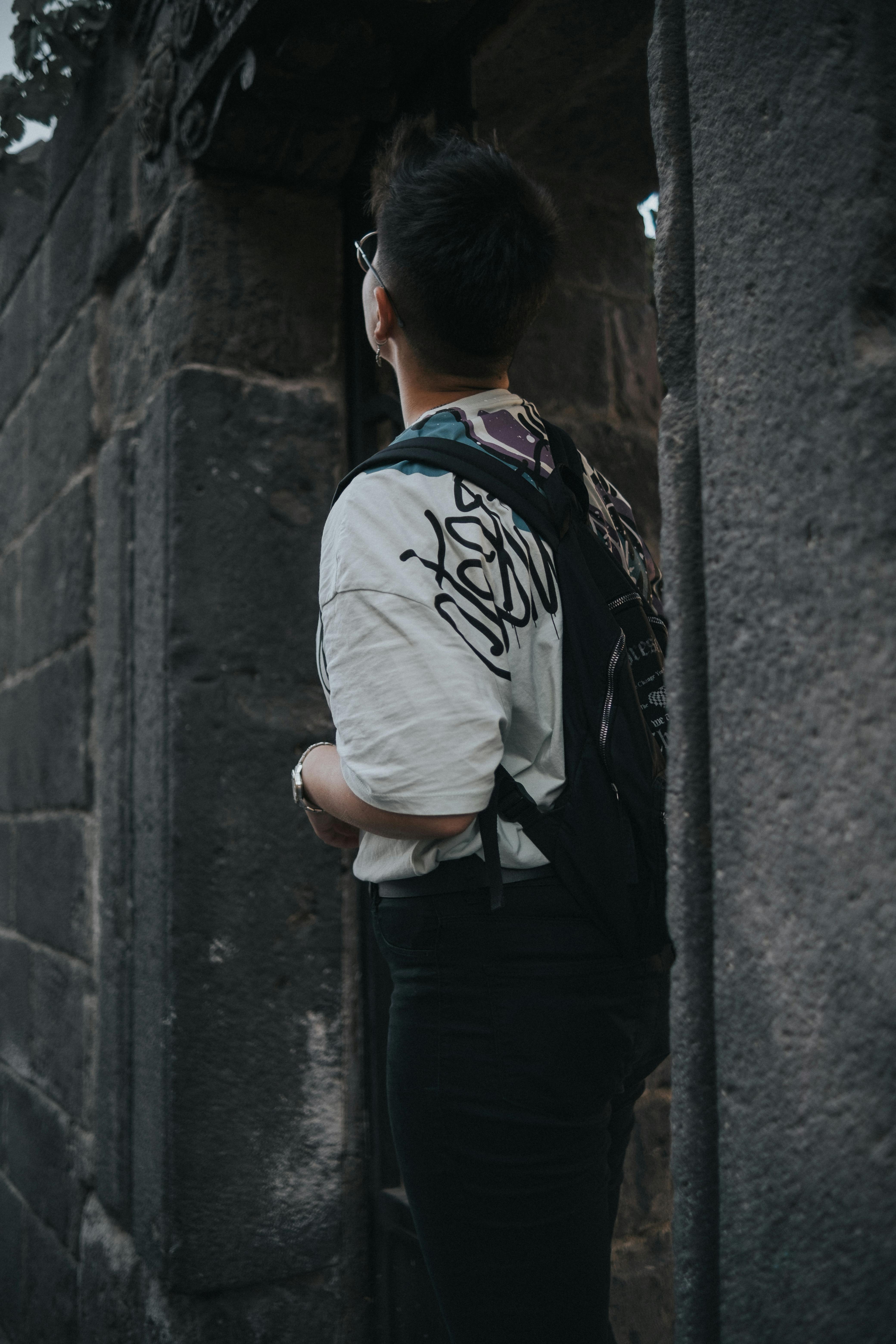 A person with a backpack stands in an ancient stone structure, looking upwards with curiosity.