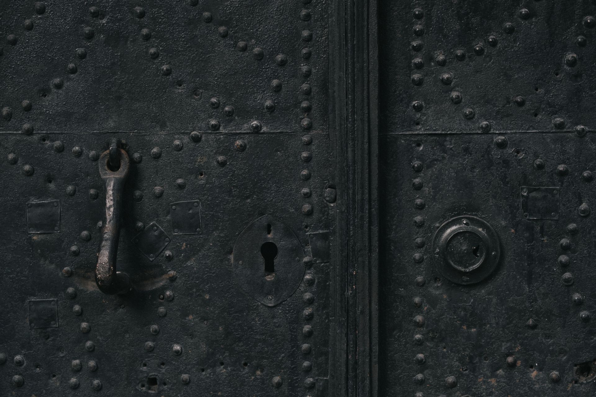 Close-up of a textured metal door with a keyhole and handle, showcasing intricate patterns.