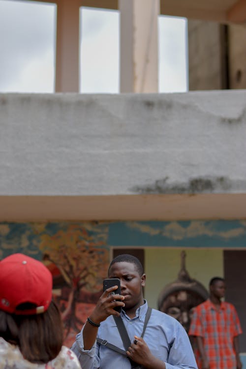 Free A black man using a smartphone in Ife, Nigeria, with mural in background. Stock Photo