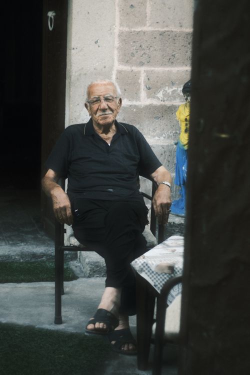 Free Senior man in black polo shirt sits relaxed outdoors by table. Stock Photo