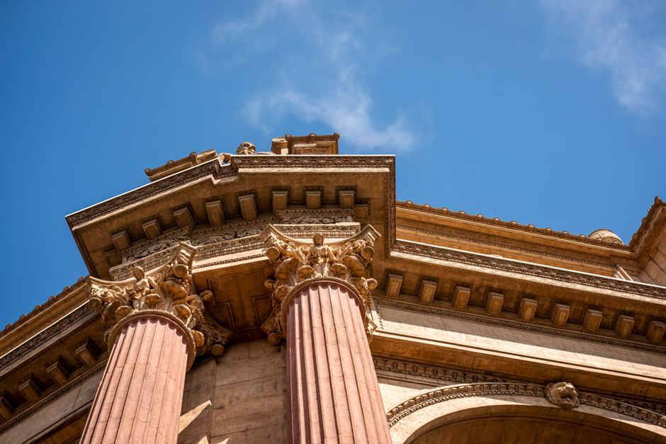 Low-angle view of magnificent Roman-style columns under a vibrant blue sky, showcasing intricate architectural details.