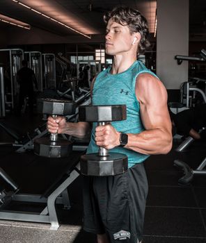 Caucasian man exercising with dumbbells in a gym for strength training and fitness.