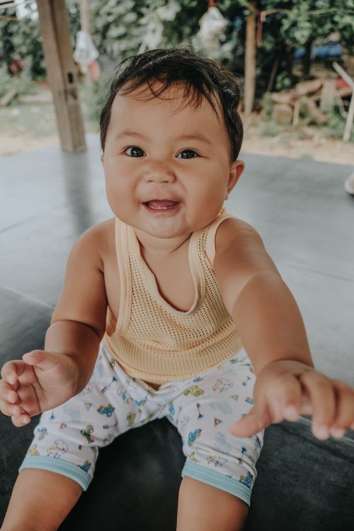 Free Adorable baby in a yellow tank top reaches out joyously indoors. Stock Photo