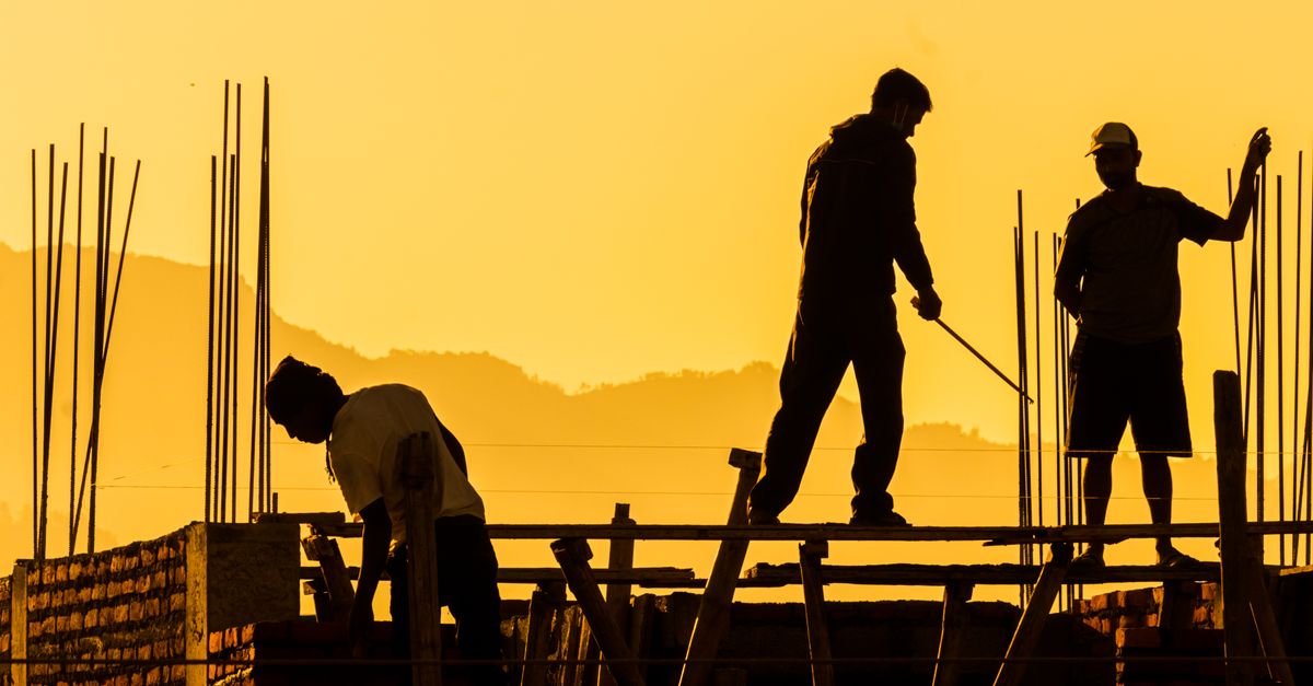 Silhouetted workers on a construction site at sunset, highlighting the manual labor involved.