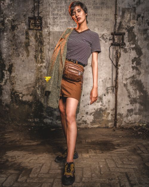 Free A fashion-forward woman in a striped shirt and skirt poses confidently in a rustic urban setting. Stock Photo