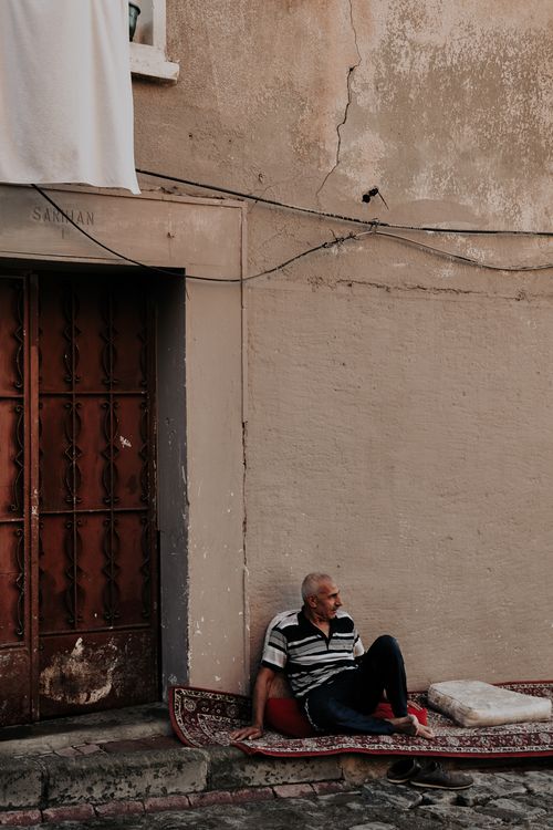 Free An elderly man sitting on a rug against a wall in an urban street in Istanbul, Turkey. Stock Photo