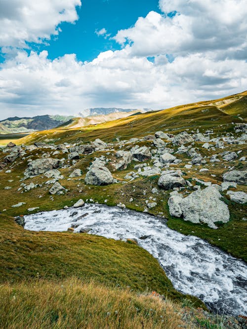 River Flowing on Green Grass Near Rocks and Mountains