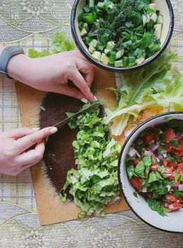 Hands chopping fresh vegetables for salad on a wooden board. Vibrant and healthy ingredients.