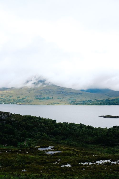 Free Breathtaking view of a mountain partially covered by clouds, overlooking a serene lake. Stock Photo