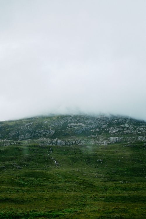 Free A serene view of a misty mountain with lush green fields and a foggy sky above. Stock Photo
