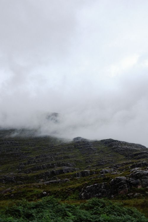 Free A captivating view of a mist-covered green mountain with rocky terrain and white clouds. Stock Photo