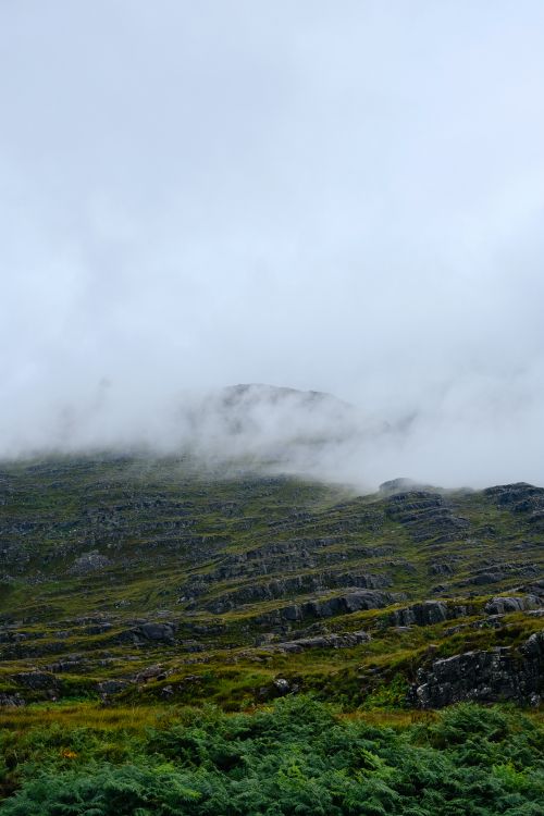 Free A serene foggy mountain landscape with lush green foreground and rocky peaks shrouded in mist. Stock Photo