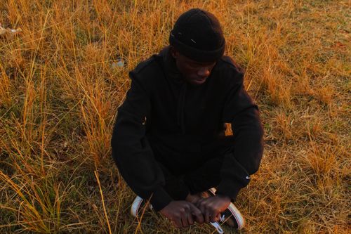 Free A man in a beanie and black jacket sits peacefully on dry grass in an autumn setting. Stock Photo