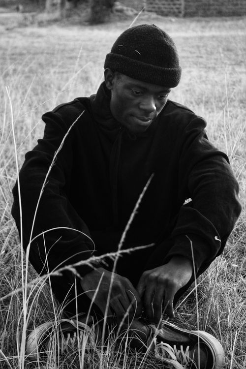 Free Black and white portrait of a man seated in a grassy field wearing a beanie. Stock Photo