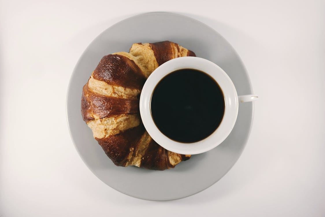 Croissant on Ceramic Plate Beside Cup With Coffee