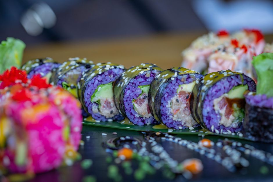 A bowl of steamed purple sticky rice with deep violet grains studded with a few white grains, served alongside sliced mango.
