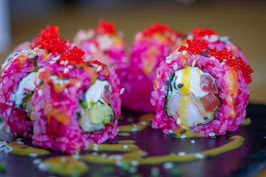 Close-up of colorful sushi rolls with pink rice, vibrant ingredients, and fish roe, garnished on slate.