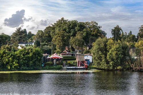 Free Charming lakeside scene with vibrant greenery and cozy houses, perfect for summer relaxation. Stock Photo